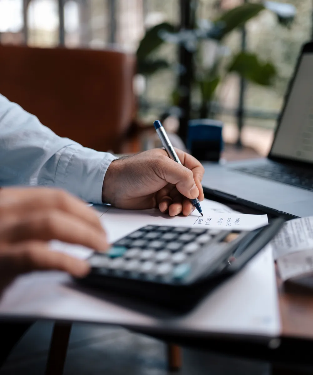 An accountant writing figures beside a desk calculator in a bright office